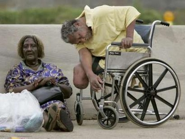 Photo of an African American man with no legs sitting in a wheelchair at the side of the road.