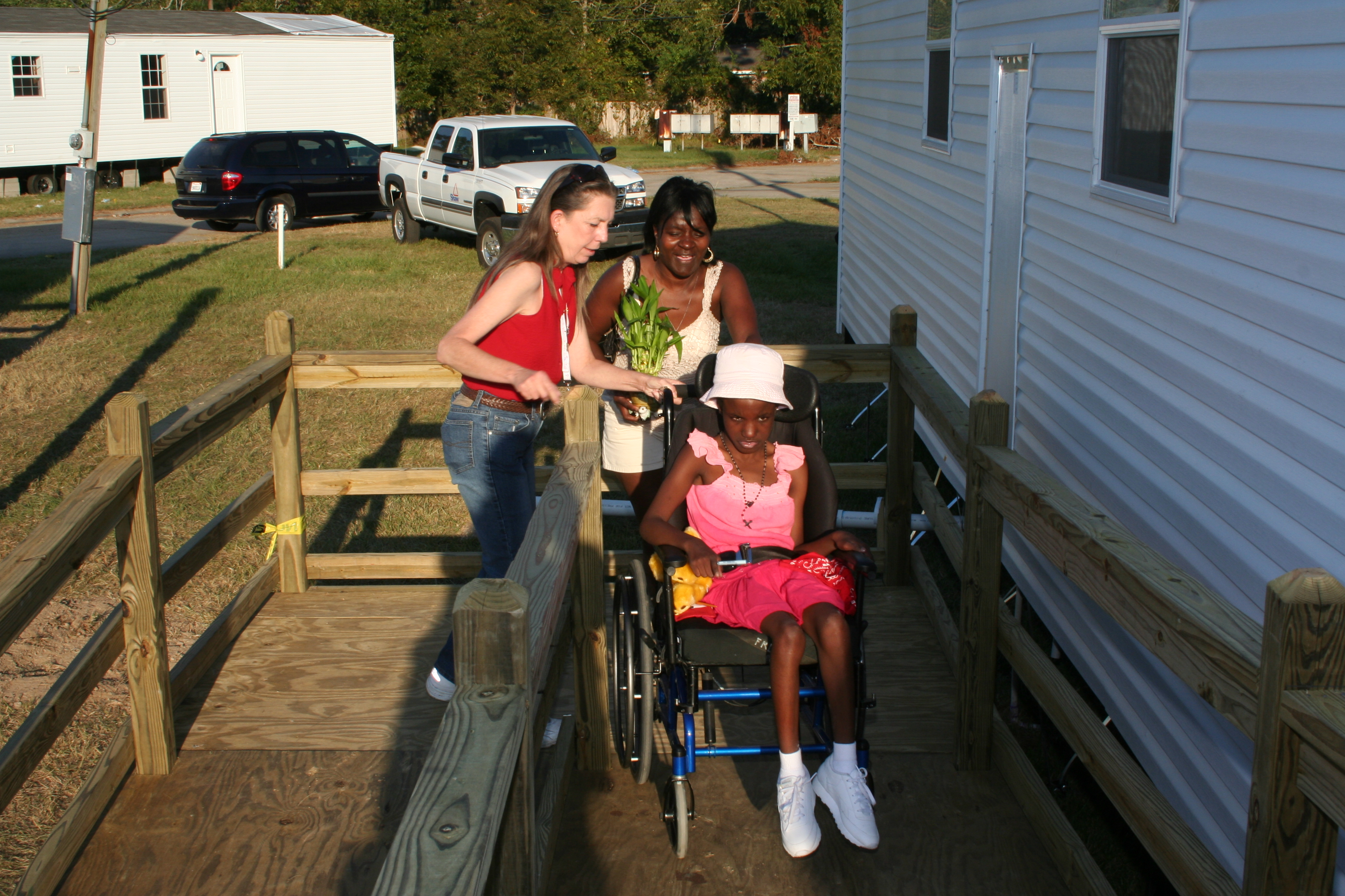 A woman pushes her daughter in a wheelchair up a ramp into their new accessible mobile home.