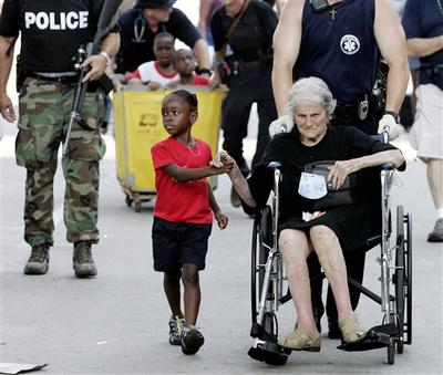 A young African American child holds the hand of an elderly white woman in a wheelchair.