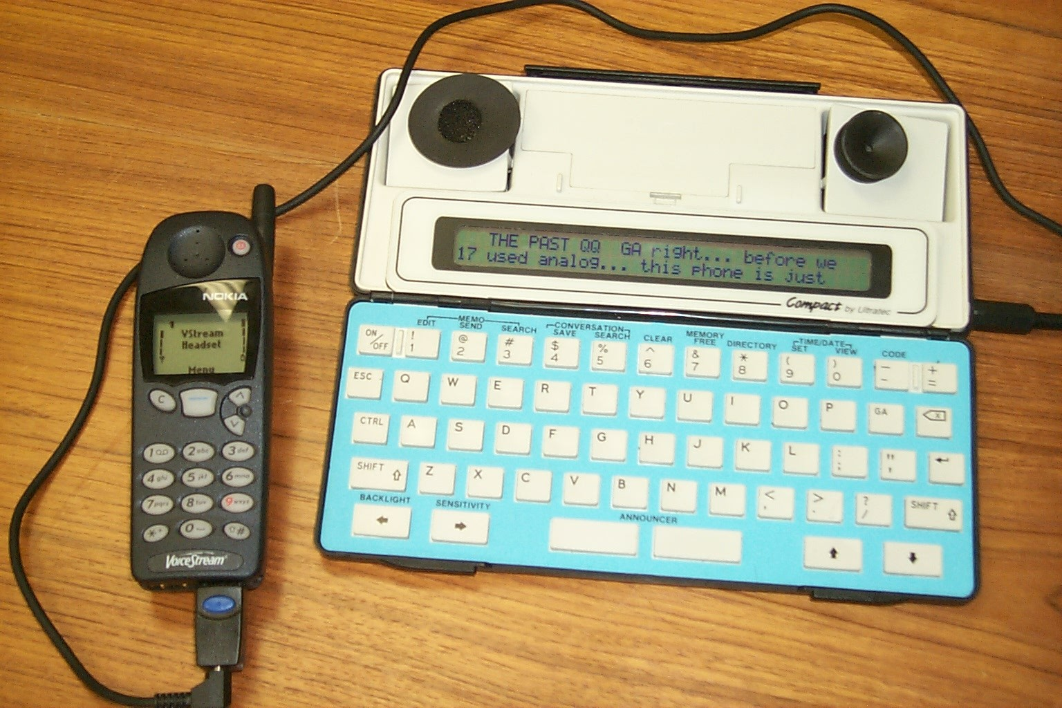Image of a cell phone connected by a cable to a portable TTY.