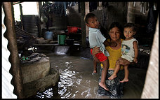 Photo of a woman holding two small children in flooded home.