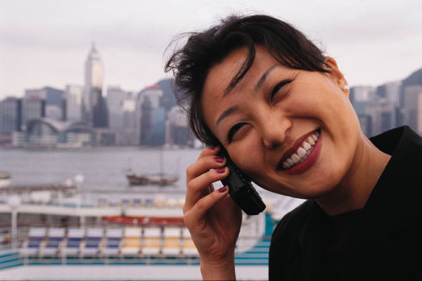 Photo of a smiling Asian woman holding a wireless phone up to her ear.