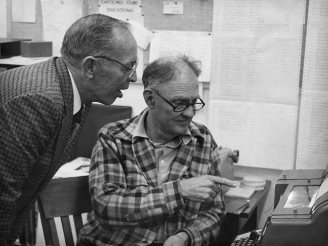 Black and white photo of Robert Weitbrecht showing his TTY modem to another man.