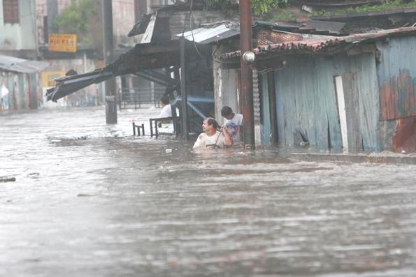 Woman stands in chest deep water in the middle of a flooded town.
