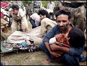 A man cradling a young child in his arms, with other injured people in the background.
