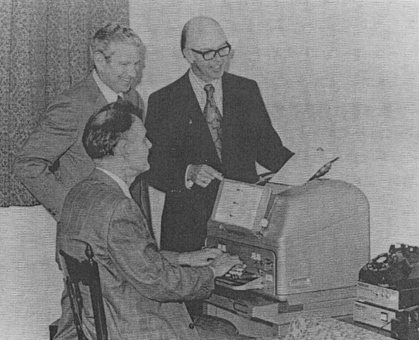 Black and white photo of Weitbrecht, Saks, and Marsters sitting in front of an old TTY.